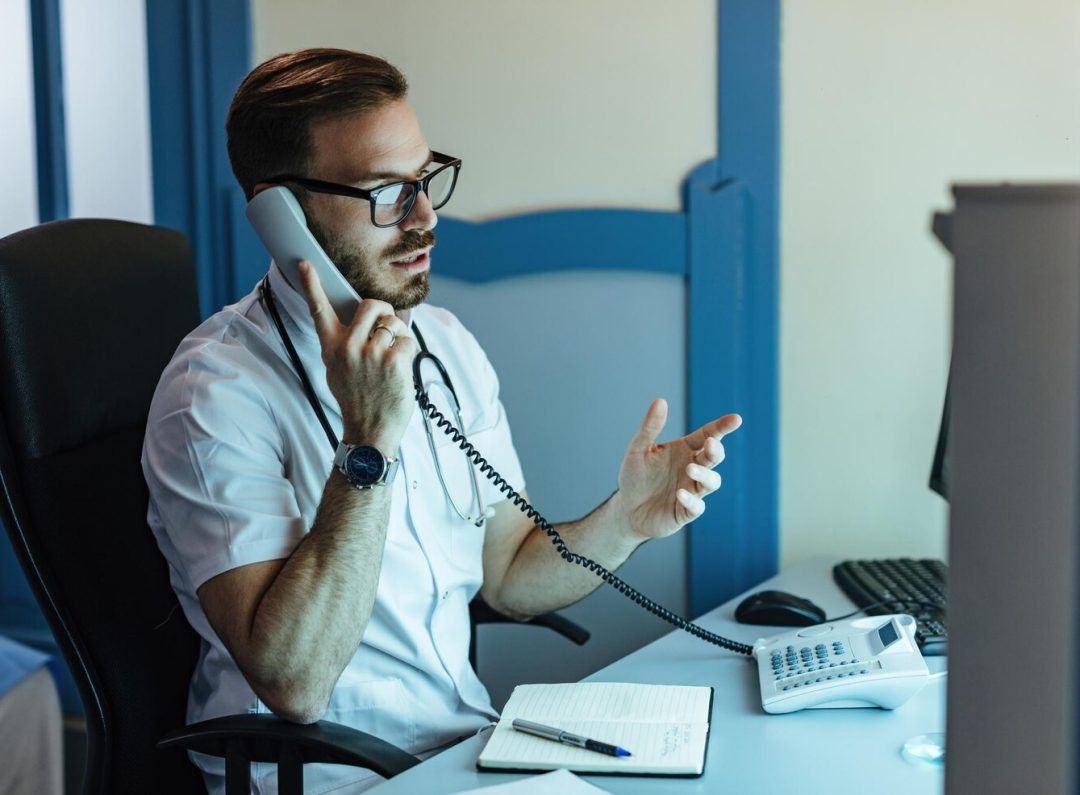 male-doctor-sitting-his-office-communicating-with-someone-phone_637285-5208